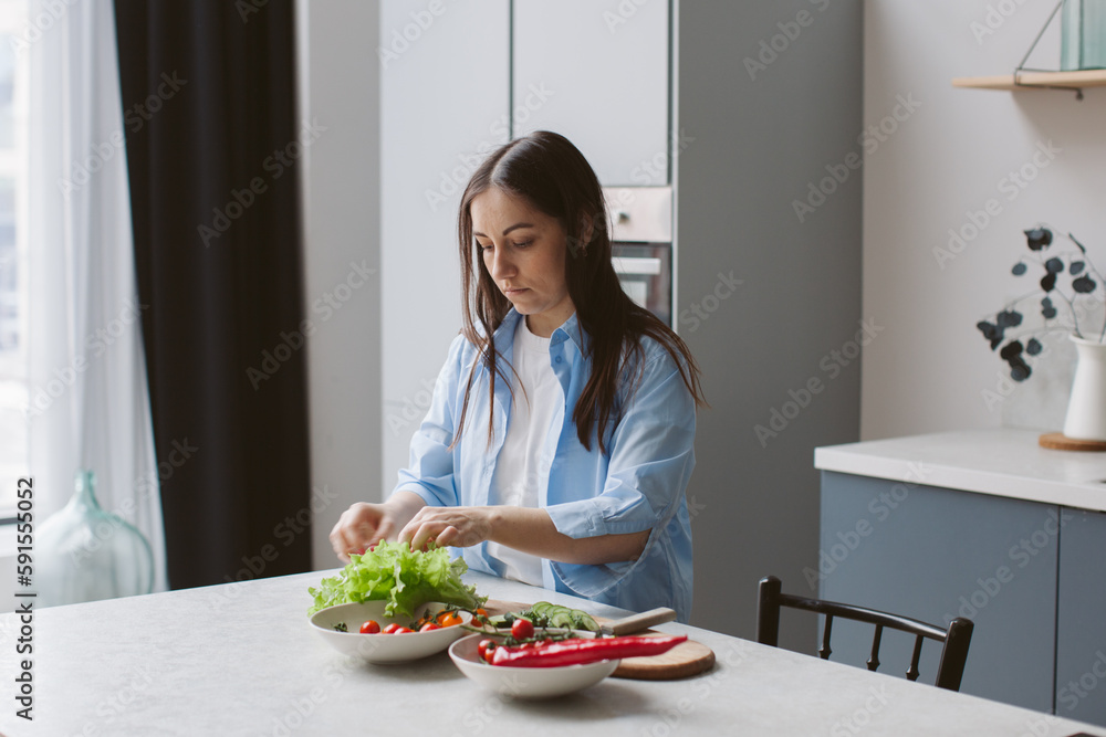A woman prepares a salad in the kitchen. Cooking and health care.