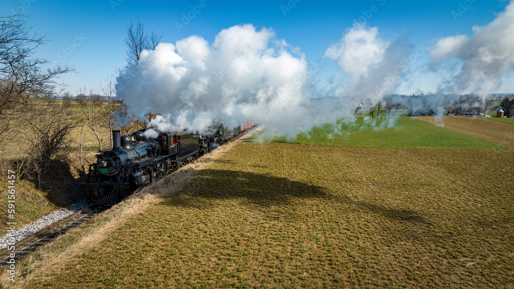 Obraz premium An Aerial View of a Steam Double Header Freight and Passenger Train, Traveling Thru Farmlands, Blowing Smoke, on a Winter Day