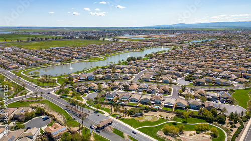 Drone photos over The Lakes community in Discovery Bay, California with houses, houses with solar, a lake with fountains, roadways and a beautiful blue sky with room for text
