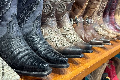 Collection of cowboy boots stand on a wooden shelf in store in texas, western shoes at ranch.