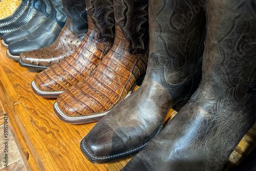 Collection of leather handmade cowboy boots stand on a wooden shelf in store in texas, western shoes at ranch.