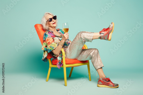 Funny old woman, chilling and relaxing in an armchair, drinking wine. Generative AI.