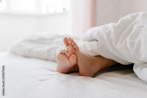 Feet of little girl on bed under white blanket, sleep at morning.