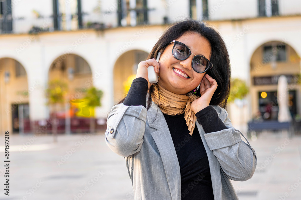 Fototapeta premium Smiling young Asian business woman looking at camera, listening to music with wireless headphones.