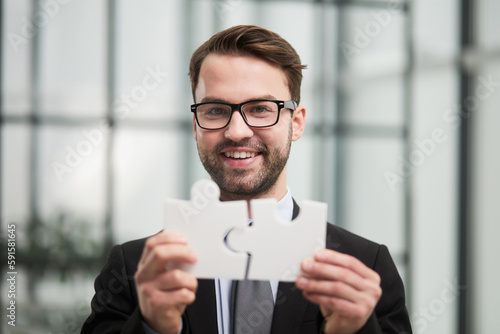 Portrait of optimistic bearded businessman holding puzzle pieces, solving tasks, looking at camera