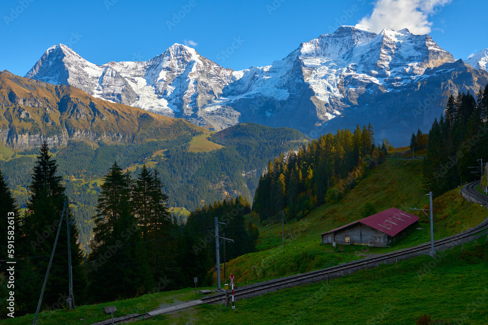 Mountain view of Jungfrau, Monch, Eiger peaks at sunset with old barn and railroad in Switzerland Bernese region.