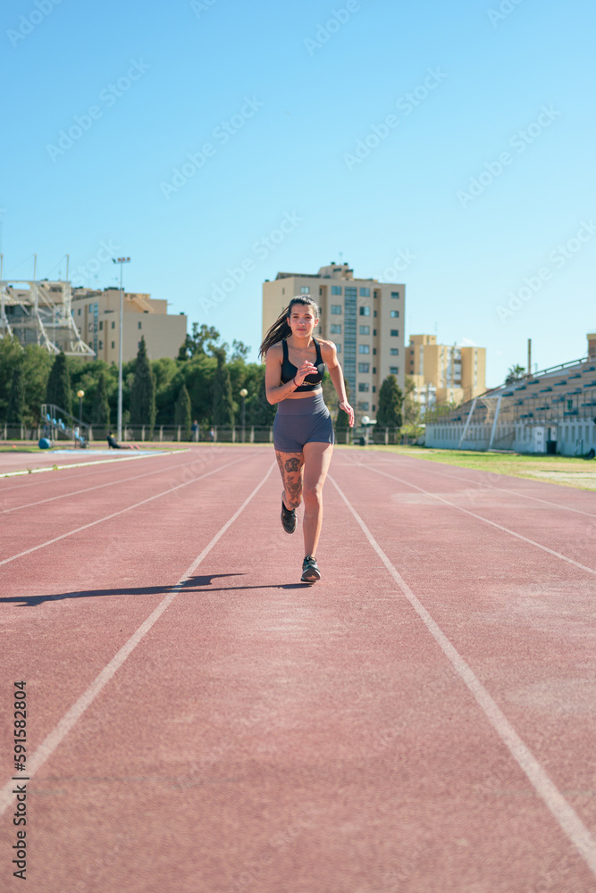 Young athletic girl with tattoos runs around a running track