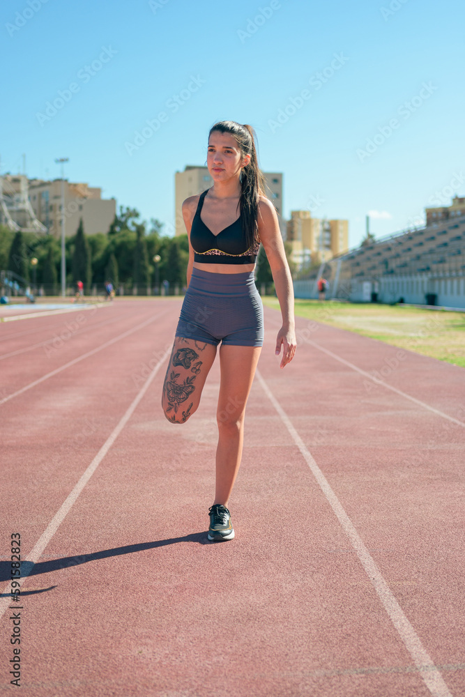Female athlete with tattoos performs stretching on a running track