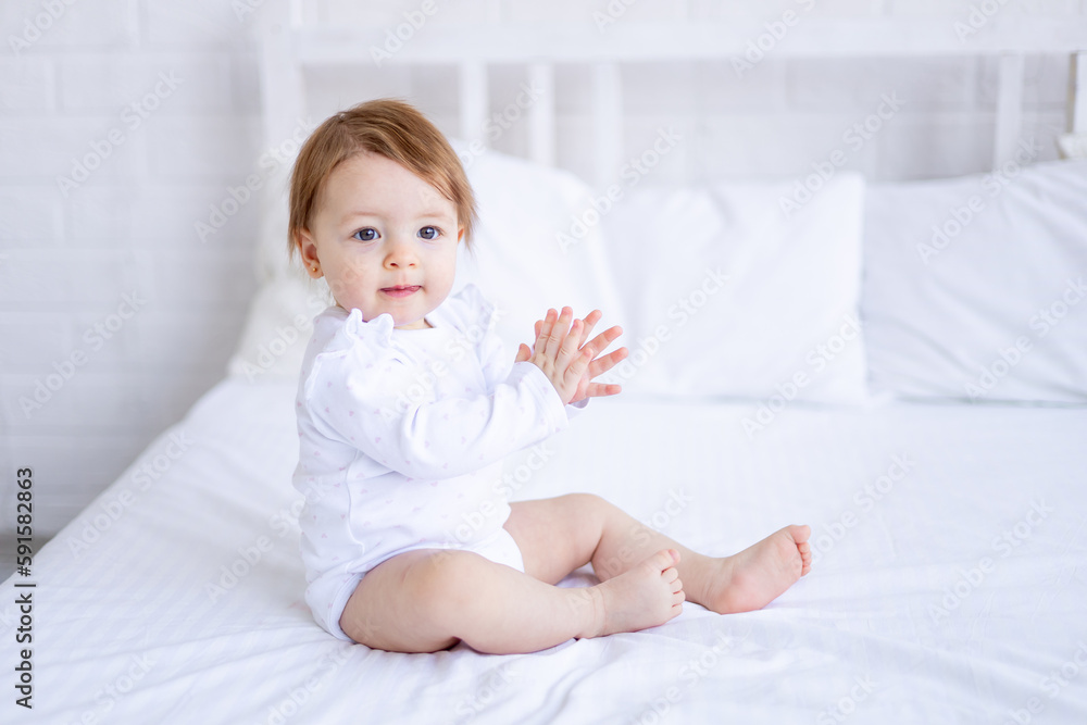 funny baby girl of six months on a bed in white clothes smiling, clapping her hands, a small child on a cotton bed at home woke up in the morning after sleeping, the concept of children's goods funny baby girl of six months on a bed in white clothes smiling, clapping her hands, a small child on a cotton bed at home woke up in the morning after sleeping, the concept of children's goods