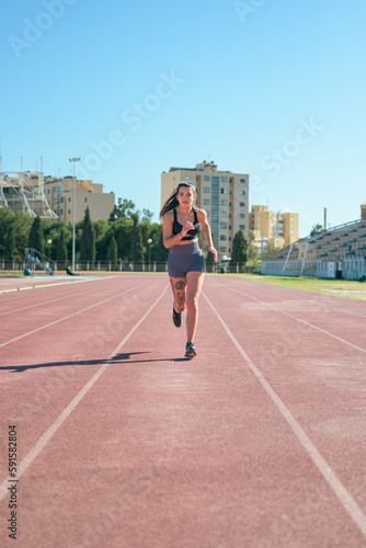 Young athletic girl with tattoos runs around a running track