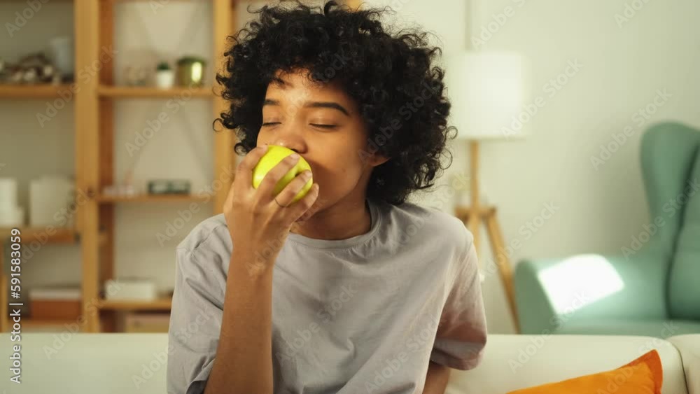 Happy pretty girl biting green apple at home. Beautiful african american young woman eating fresh fruit and smiling. Healthy food vegan vegetarian dieting concept. Healthy snack clean food Happy pretty girl biting green apple at home. Beautiful african american young woman eating fresh fruit and smiling. Healthy food vegan vegetarian dieting concept. Healthy snack clean food