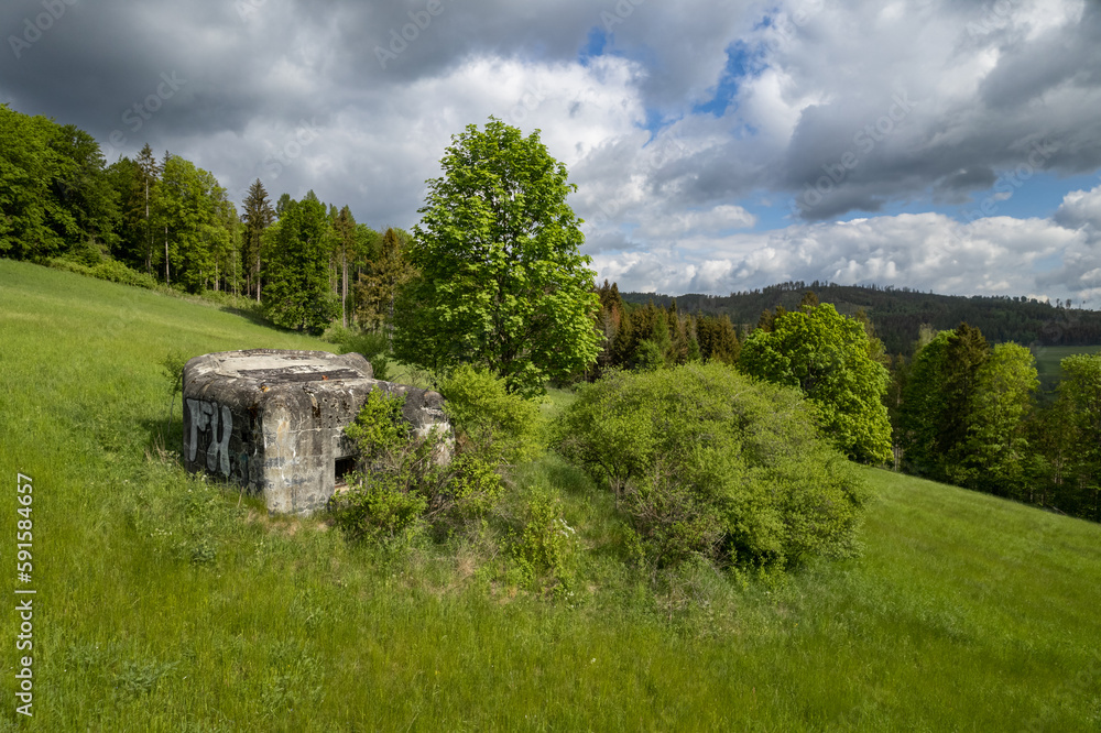 A former military concrete bunker in a meadows with dark clouds and forest. Jeseniky, Czech republic.