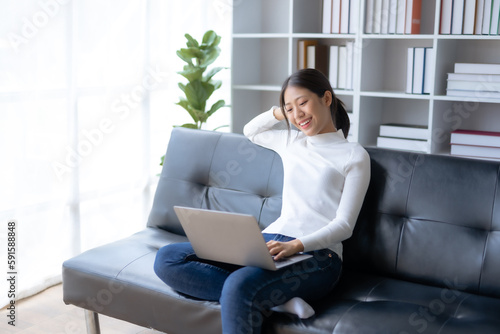 Happy young Asian woman relaxing using laptop computer on sofa at home.