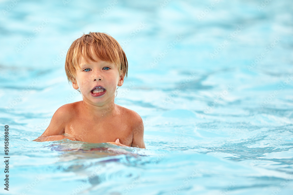 Little boy in the pool with a displeased face, surprised kid in the water of the pool, copy space.