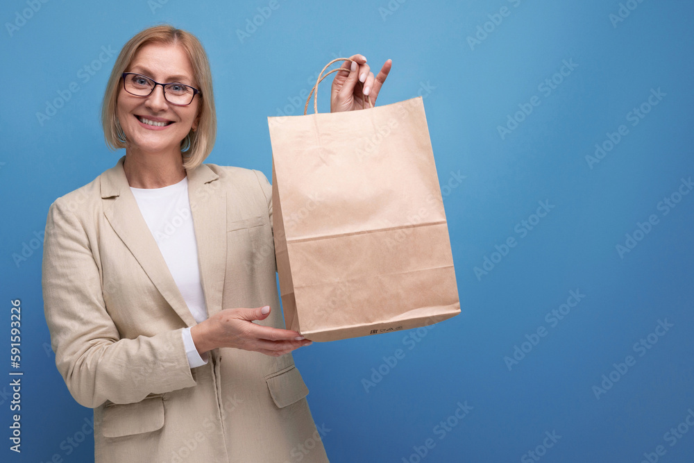 middle-aged business concept. smiling woman in jacket holding package on studio background with copy space