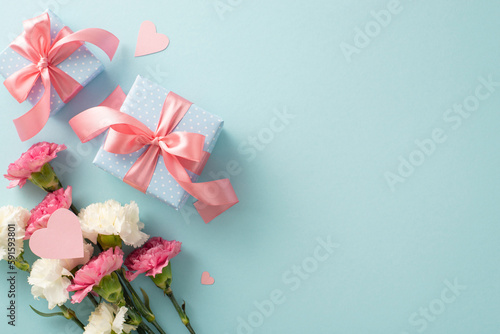 Top flat lay photo of beautiful present boxes with pink ribbon, carnation flowers with pink paper hearts on pastel blue background with empty space for text or advert © ActionGP