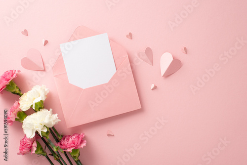 Top view stylish flat lay photo of open envelope with blank card, pretty carnation blooms, and pink paper hearts on a soft pink background © ActionGP
