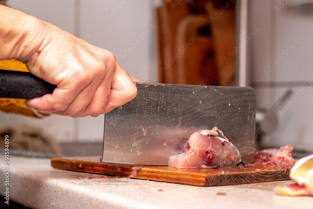 A woman cuts fish with a large knife at home in the kitchen A woman cuts fish with a large knife at home in the kitchen