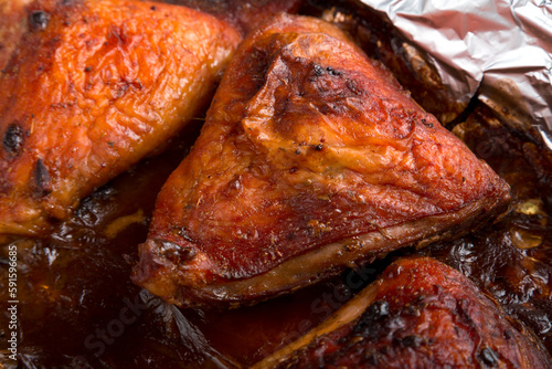 Baked chicken thigh in spices and crispy sauce on foil close-up.