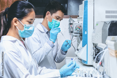 Scientist man injects sample with micro syringe into Mass Spectrometer to analyze samples, scientist woman assisted preparing samples for analysis. Mass spectrometry is used to measure mass per charge