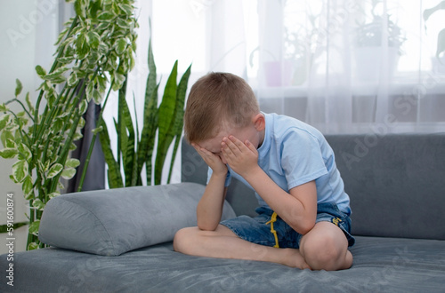 One sad little boy is sitting on couch crying and sad. Child abuse. Anxiety and stress. Concept of bullying, depressive stress. An unhappy child sitting alone