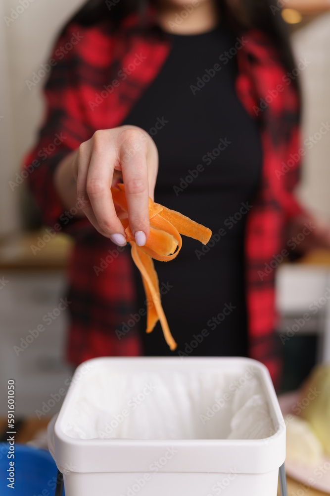 Obraz premium Woman throwing food leftovers in a compost bin. Female person recycling organic waste in a bokashi container at home. Sustainable lifestyle concept