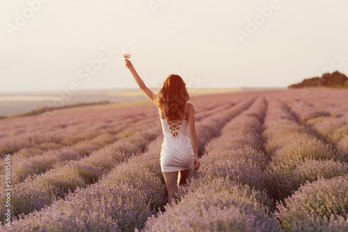 Obraz na płótnie Back view of woman in white dress holding wine glass in sunset lavender field. Provence, Southern France. w salonie