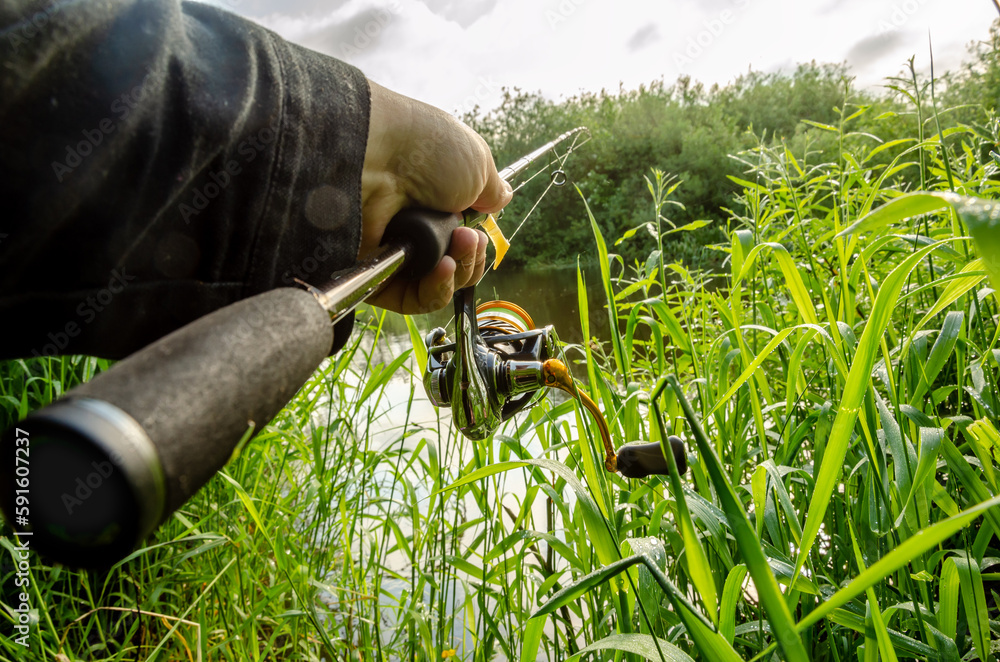 Obraz premium Male hand holding spinning rod on the background of the river.