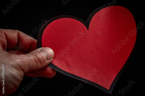 mano che regge un cuore rosso su sfondo nero photo
