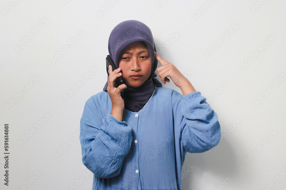 Thoughtful young Asian girl in hijab looks confused while on a phone call Thoughtful young Asian girl in hijab looks confused while on a phone call