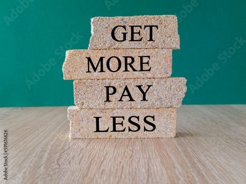 Get more pay less symbol. Concept words Get more pay less on brick blocks on a beautiful wooden table green background. Business Get more pay less concept. Copy space.