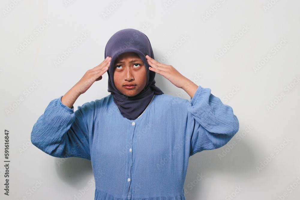 Young Asian girl in hijab grabbing her head while thinking about something Young Asian girl in hijab grabbing her head while thinking about something