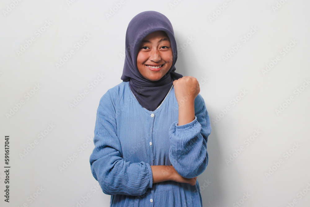 Young Asian girl in hijab raising fist, celebrating success Young Asian girl in hijab raising fist, celebrating success