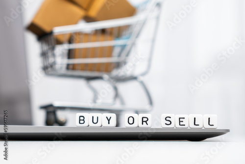 Buy yes or no words on cubes laying on the laptop and a toy shopping cart with carton boxes serves as the background.