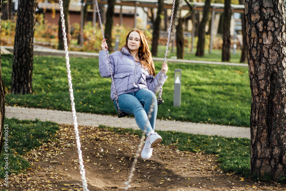 Teens Mood swings: Hormonal changes can cause mood swings, irritability, and emotional outbursts in teenage girls. Teenager girl in glasses on swing in city park.
