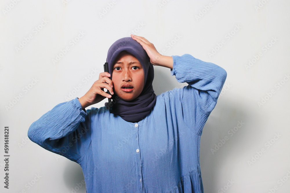 Young Asian girl in hijab looks shocked while using mobile phone Young Asian girl in hijab looks shocked while using mobile phone