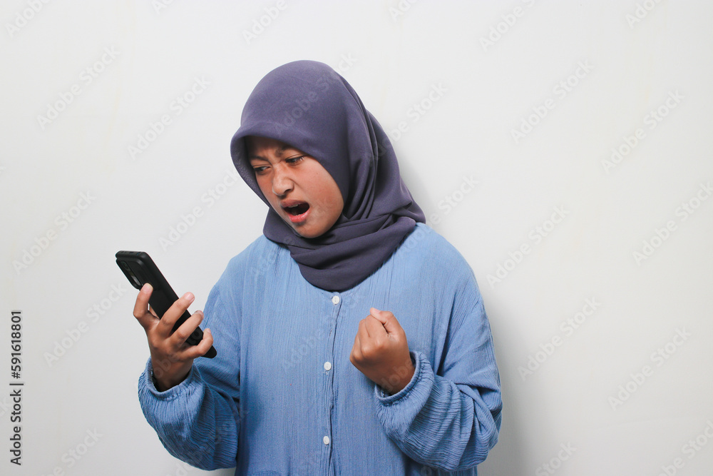 Young Asian girl in hijab is annoyed while using mobile phone Young Asian girl in hijab is annoyed while using mobile phone