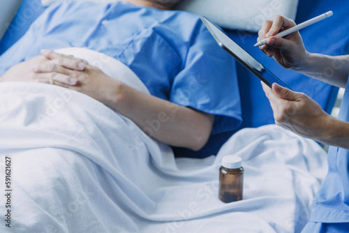 Side view of diverse doctors examining Asian female patient in bed in ward at hospital.