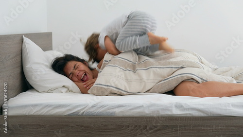 Child waking up mother in the morning bed. Little boy jumps on top of mom. Authentic real life lifestyle motherhood concept