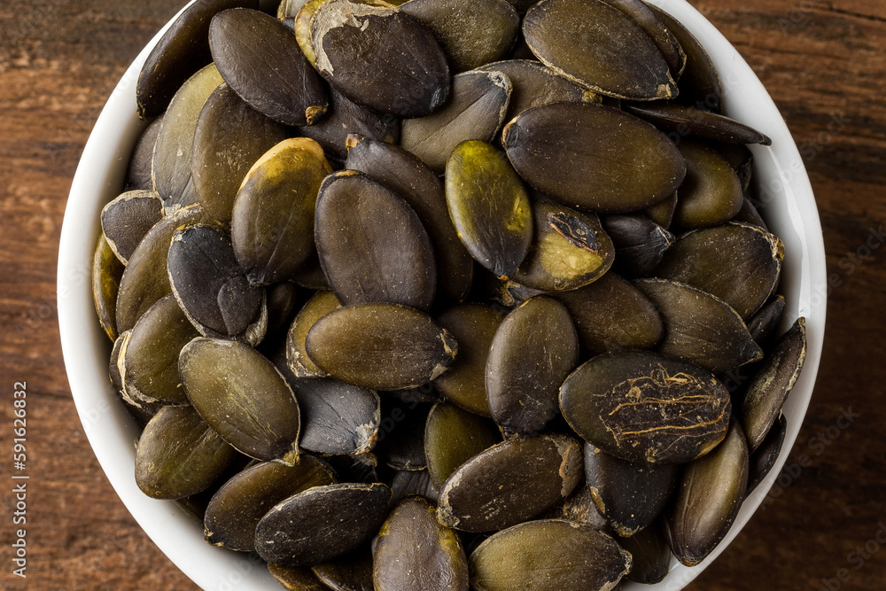Peeled pumpkin seeds in bowl on rustic wooden table. Top view Peeled pumpkin seeds in bowl on rustic wooden table. Top view