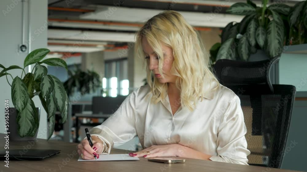 Portrait of young employee writing in notebook and speaking on mobile phone in office. Business communication and information concept Portrait of young employee writing in notebook and speaking on mobile phone in office. Business communication and information concept