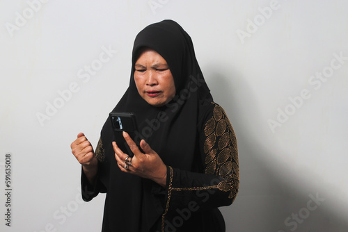 Middle aged Asian women wearing hijab feels upset while getting bad news on her phone