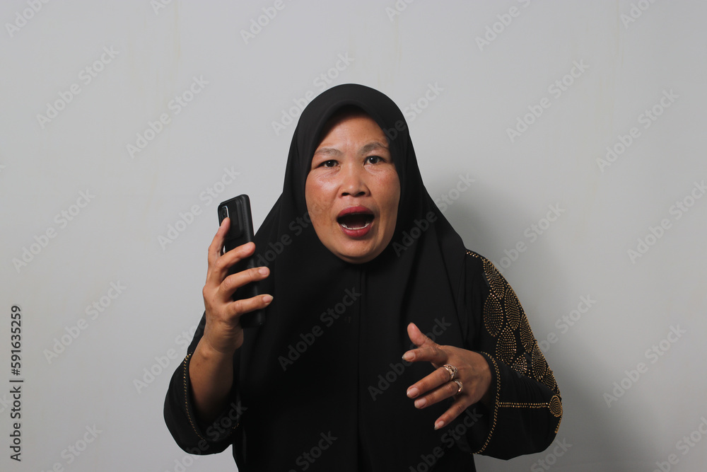 Shocked Middle aged Asian women wearing hijab reacting special offer on mobile phone Shocked Middle aged Asian women wearing hijab reacting special offer on mobile phone