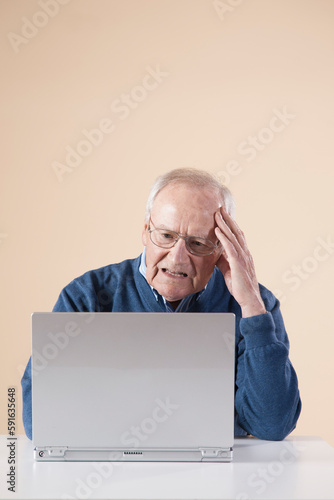 Senior Man Sitting Sitting at Table using Laptop Computer looking Confused, Studio Shot on Beige Background