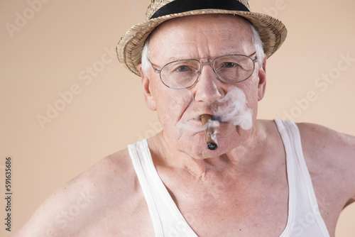 Portrait of Senior Man wearing Undershirt and Straw Hat while Smoking Cigar, Studio Shot on Beige Background