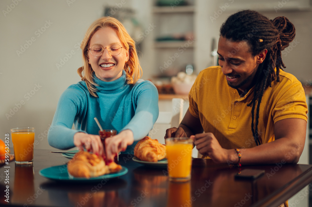 A happy interracial couple is laughing and having breakfast at home.