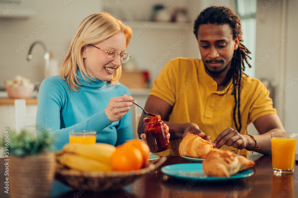 A happy multiracial couple is having breakfast at home.