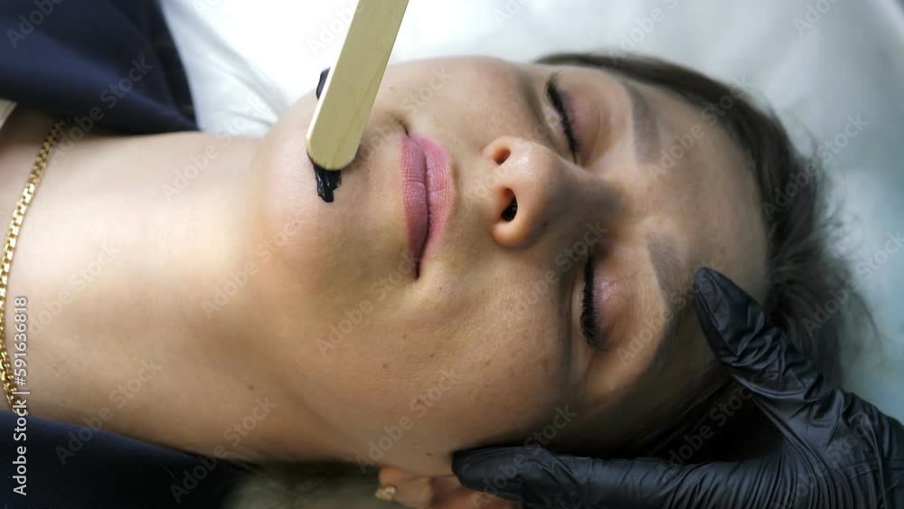 Beautician applies black mask on face of beautiful woman. Girl in spa salon doing carbon peeling procedure. Carbon peeling of the face. Skin care cosmetology. Laser therapy and skin treatment Beautician applies black mask on face of beautiful woman. Girl in spa salon doing carbon peeling procedure. Carbon peeling of the face. Skin care cosmetology. Laser therapy and skin treatment
