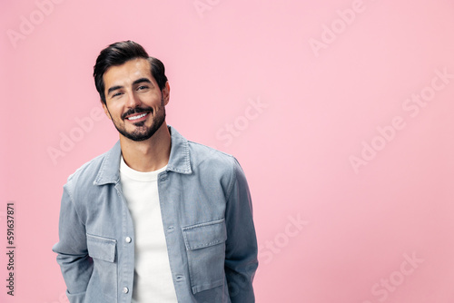 Portrait of a stylish brunette man with a beard beautiful smile on a pink background in a white T-shirt and jeans smile and joyful emotion on his face, copy space