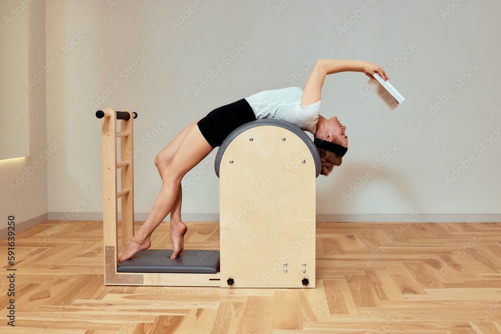 woman doing pilates exercises on reformer, woman reading a book during